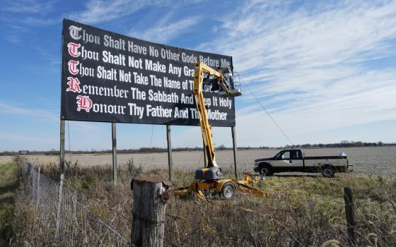 Billboard in field pictured against wide, blue sky. 