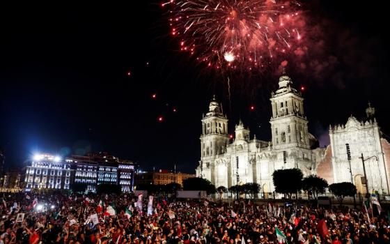 Fireworks explode in night sky over large crowd assembled in front of the Metropolitan Cathedral. 