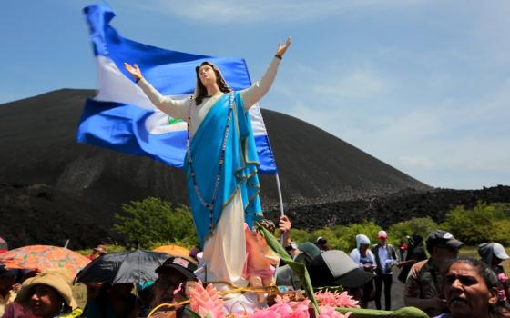 Statue of Mary and Nicaraguan flag stand above group of people.