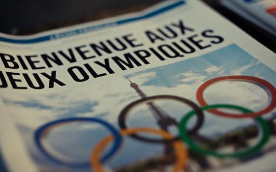 Cover of paper displays graphic of the Olympian rings superimposed over the Eiffel Tower. 