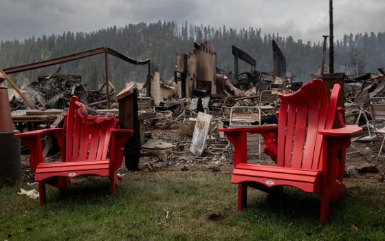 Melted lawn chairs shown in front of incinerated house and smokey, charred landscape. 