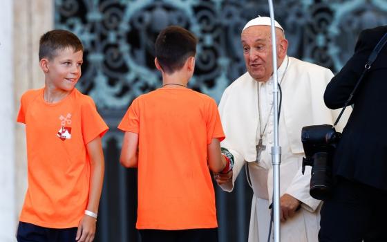 Pope Francis, standing, bends to shake the hand of a young altar server. 