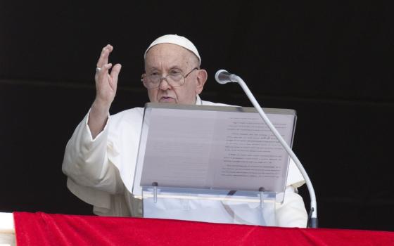 Pope at lectern with hand raised in blessing. 