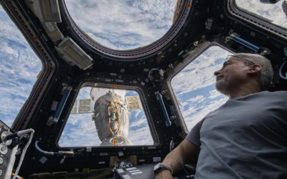 Astronaut in spacecraft looks out window at earth. 