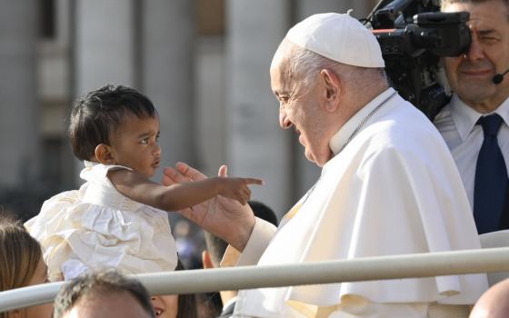 Small child holds out arm as Pope smiles.