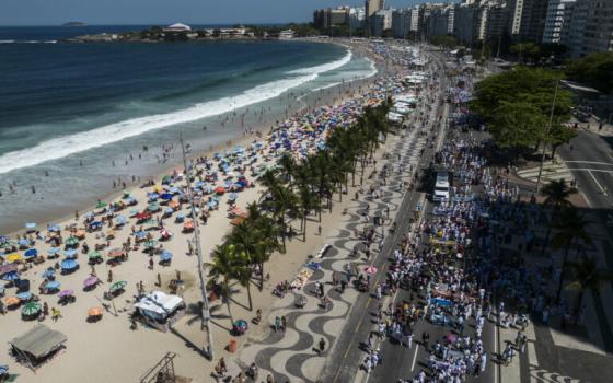 Aerial view of large assembly marching alongside beach. 