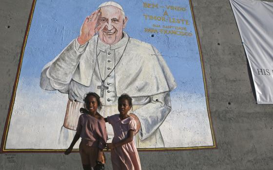 Two young children stand beneath large mural of Pope Francis.