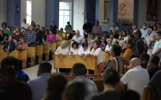 People in pews praying in a very full church.