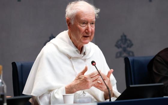 Radcliffe wearing white habit of the Dominicans, sits at table speaking.