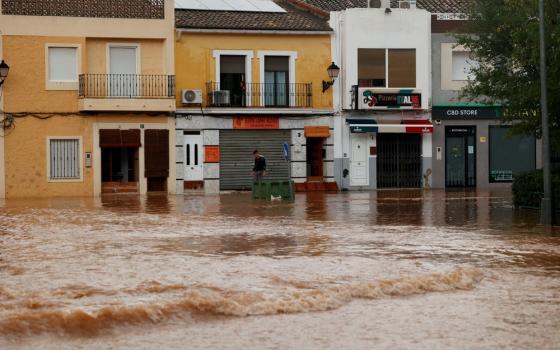 Street runs with a river of brown water past low, attached buildings.