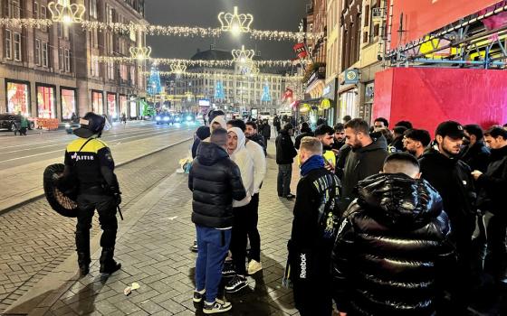 People stand on street wearing coats, assembled are police.