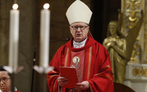 The bishop is vested for mass in red, wearing mitre, and delivering remarks.