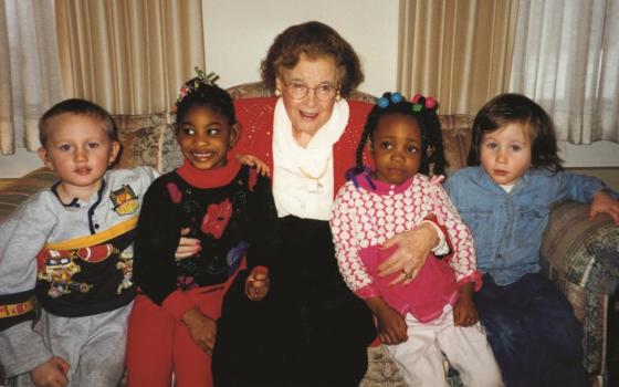 Barber sits on a couch, smiling, with two children on each side. 