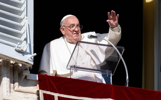 The pope stands at lectern in window and waves to people. 