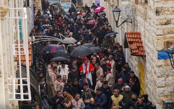 Narrow, antiquated street depicted aerially, and filled with clergy and faithful.