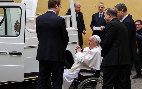 Francis seated in wheelchair, and surrounded by Mercedes reps, looks at new popemobile.