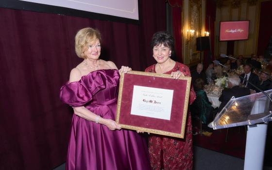 Benson wears gown and receives large framed certificate from another woman wearing gown. 