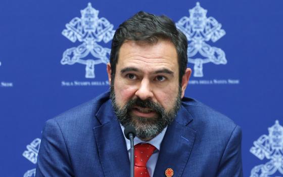 Cervantes pictured sitting at press conference wearing blue suit and red tie. 