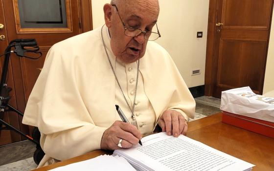 Francis sits at desk marking pages with pen. 