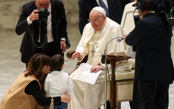 Francis seated smiles and talks to small child.