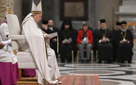 Francis vested and wearing mitre shown in profile sitting on white chair.