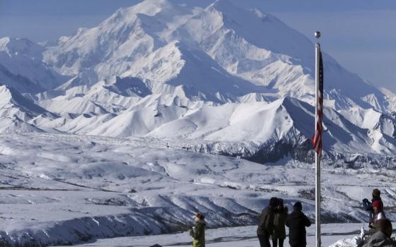 Peak in background, foregrounded are group of people and U.S. flag.