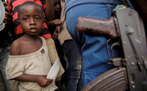 Young boy framed by the hips and legs of adults, police man's large gun foregrounded.