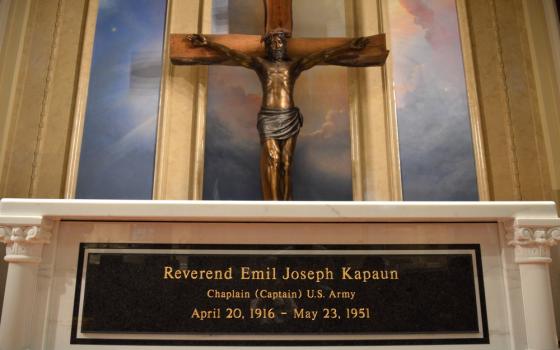 Large bronze crucifix hangs over marble tomb bearing plaque.