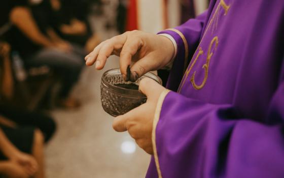 Someone grabs a pinch of ashes from a bowl full of ashes at an Ash Wednesday Mass.