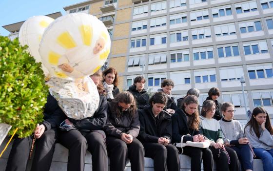 Young people and members of the House of Mary, groups associated with the Pontifical Academy of the Immaculate Conception, pray around a statue of St. John Paul II outside Rome’s Gemelli hospital March 2, 2025. Pope Francis is receiving treatment there for double pneumonia. (CNS photo/Lola Gomez)