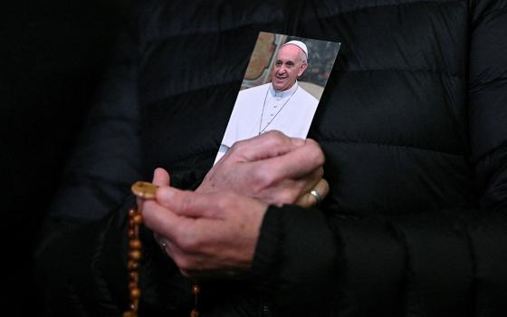 A person holds a picture of Pope Francis and a rosary during a prayer service in St. Peter's Square at the Vatican on Feb. 25, as Pope Francis continued his hospitalization. (OSV News/Reuters/Dylan Martinez)