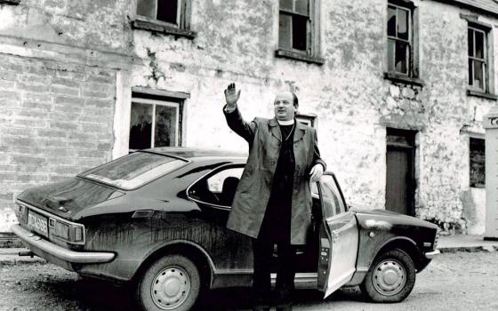 Priest stands by car and waves.