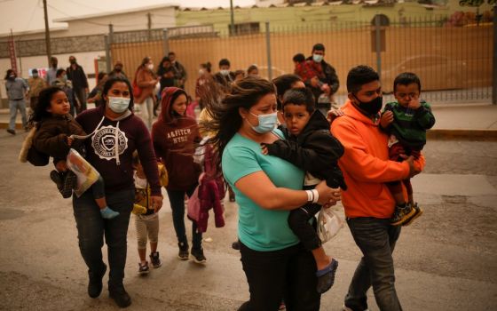 People from Central America wearing masks and carrying children outside near the Paso del Norte international border bridge in Ciudad Juárez, Mexico