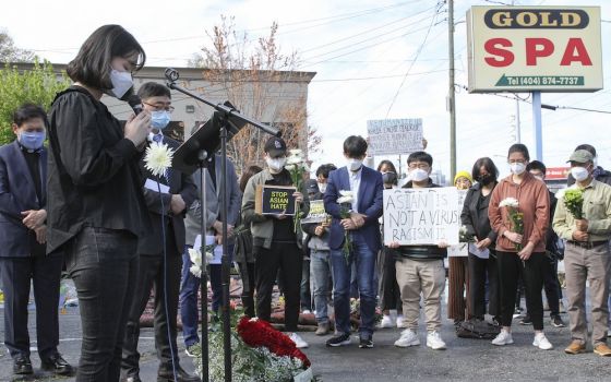 A group of mostly Asian and Pacific Islander people gather outside under a sign reading "Gold Spa" to pray