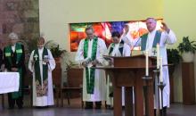 Dolan, vested only in choir robe and stole, stands at lectern with arms raised in blessing.