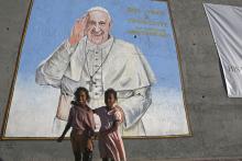 Two young children stand beneath large mural of Pope Francis.