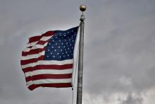 Tattered American flag against cloudy sky (Unsplash/Kevin Luke)