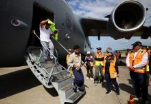 Two men step off of plane onto tarmac awaited by people wearing orange reflective vests.